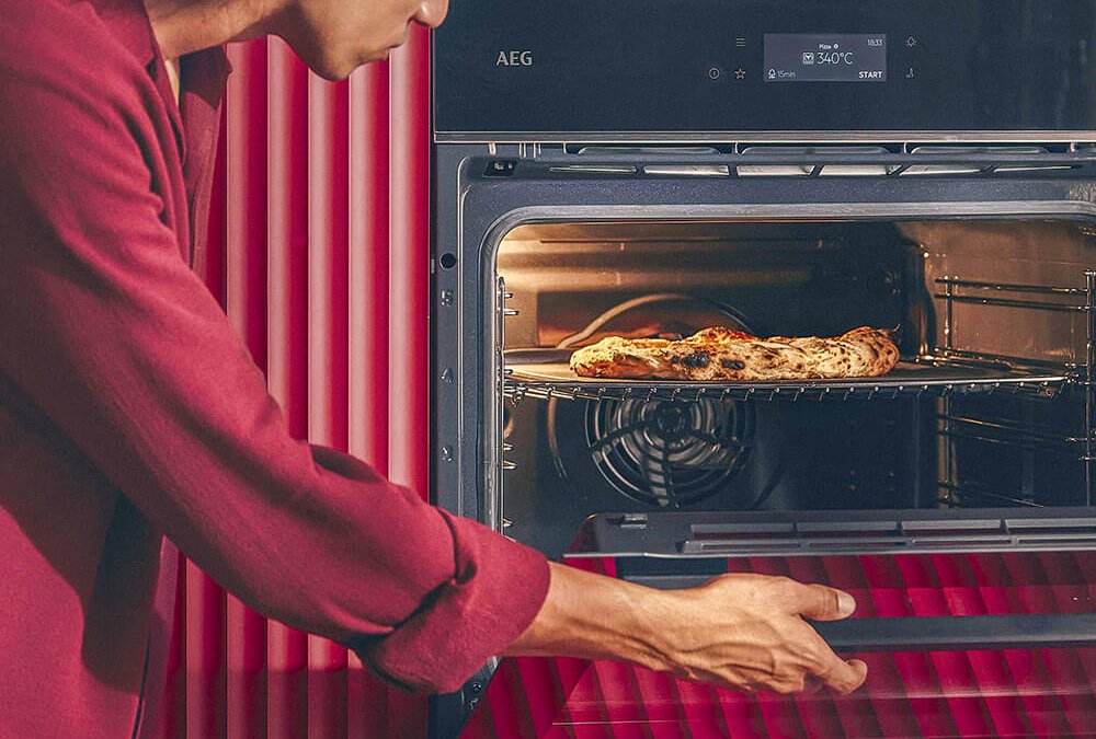 Person hält eine Pizza Margherita über einem Tisch mit weiteren Pizzen