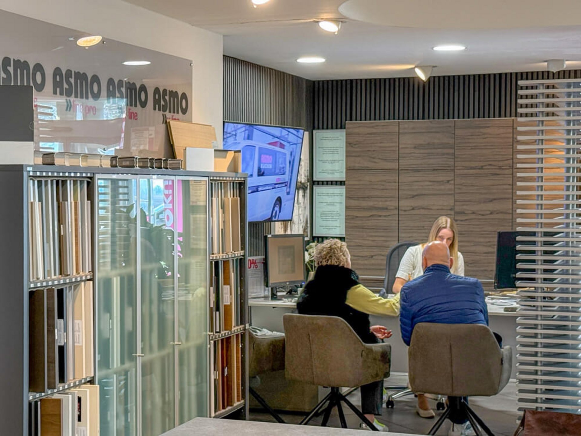 Beratungsgespräch mit drei Personen an einem Tisch im ASMO-KÜCHEN-Küchenstudio zwischen Materialmustern