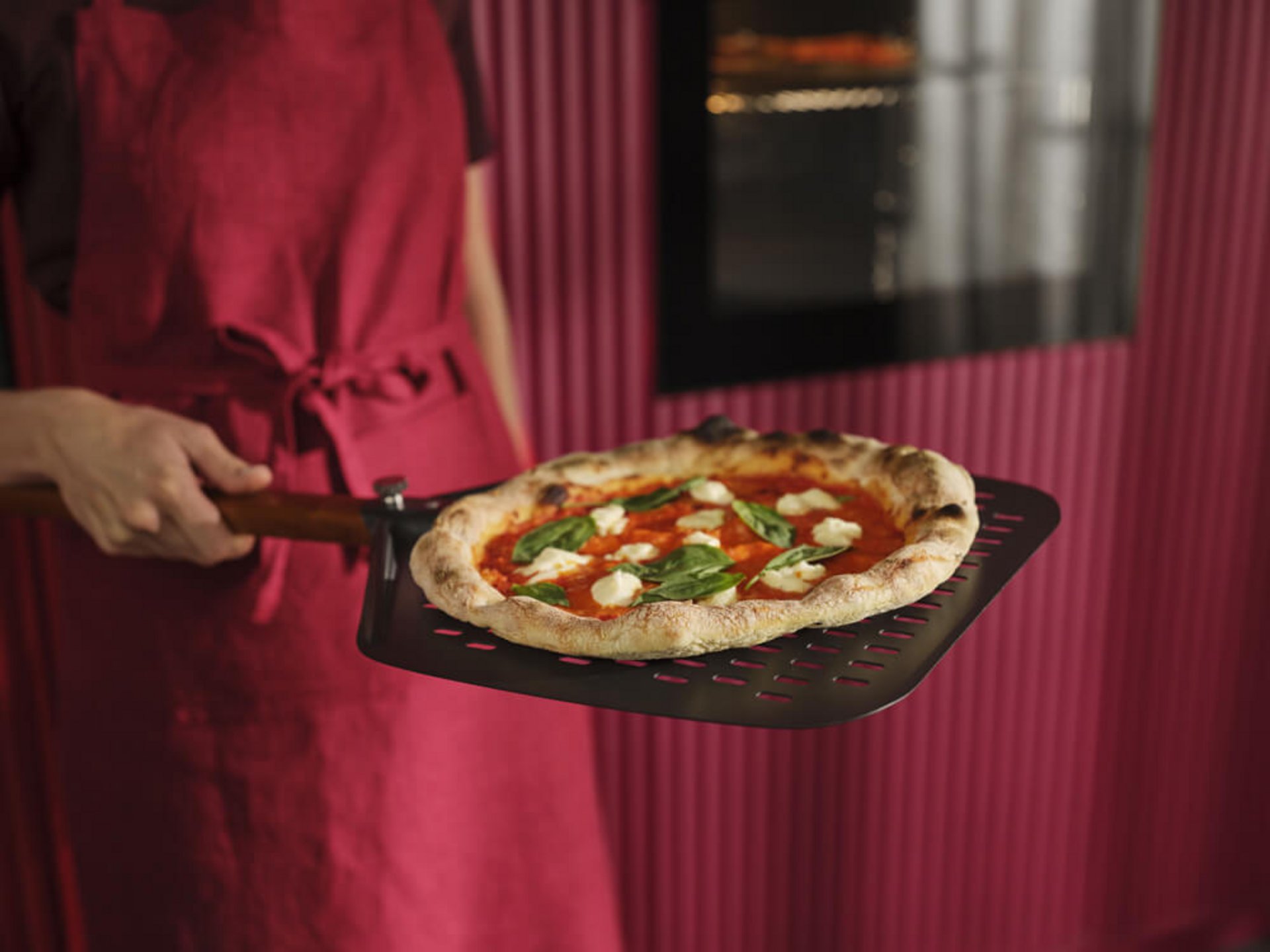 Frau hält eine gebackene Pizza Margherita auf einem perforierten Pizzaschieber