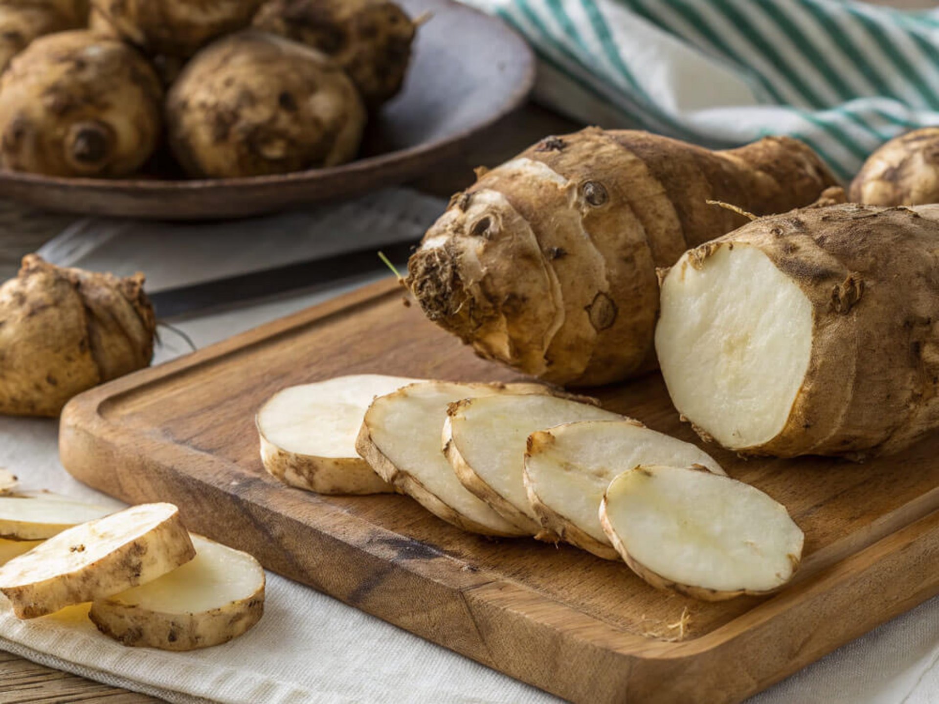 Aufgeschnittene Topinambur-Knolle und Scheiben auf Schneidebrett – zeigt, wie man Topinambur zubereiten kann.