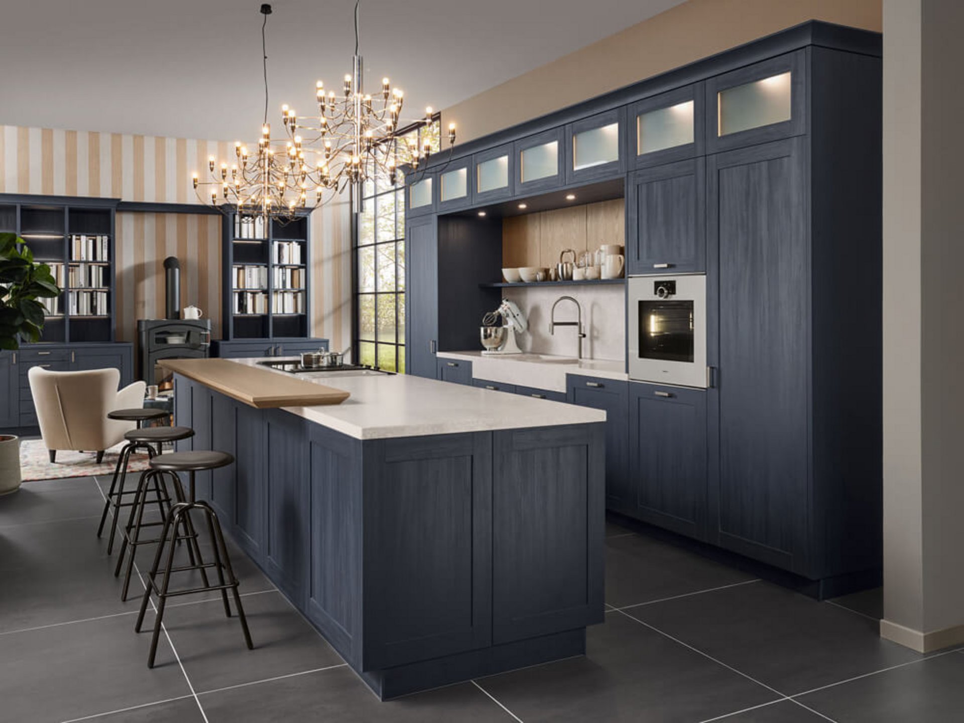 Indigoblaue Landhausküche mit Kochinsel, angesetzter Holztheke, heller Arbeitsplatte und einer Hochschrankwand mit beleuchteten Glasfächern.
