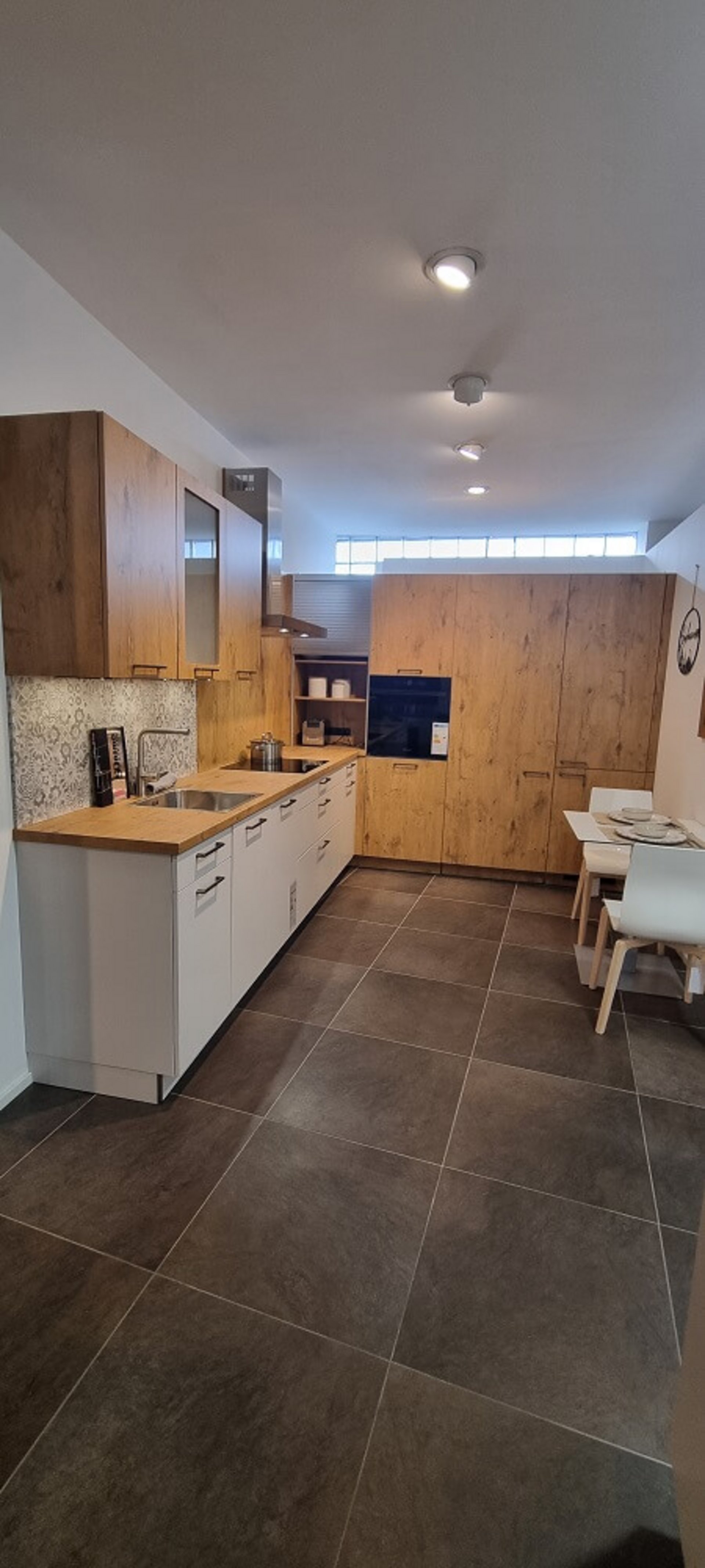 Moderne Küche Cantania in Eiche hellgrau mit weißer Unterschrankzeile, durchgehender Arbeitsplatte und Hochschrankwand im Studio von ASMO KÜCHEN Landshut.