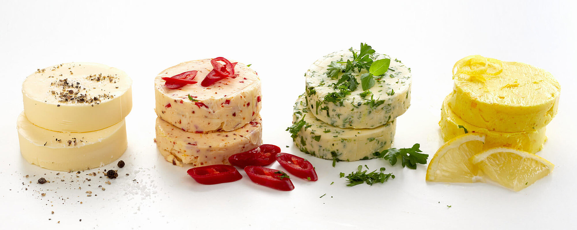 Vier verschiedene selbstgemachte Grillbutter, darunter Kräuter-Butter, Chili-Butter, Zitronen-Butter und einfache Butter mit Pfeffer.