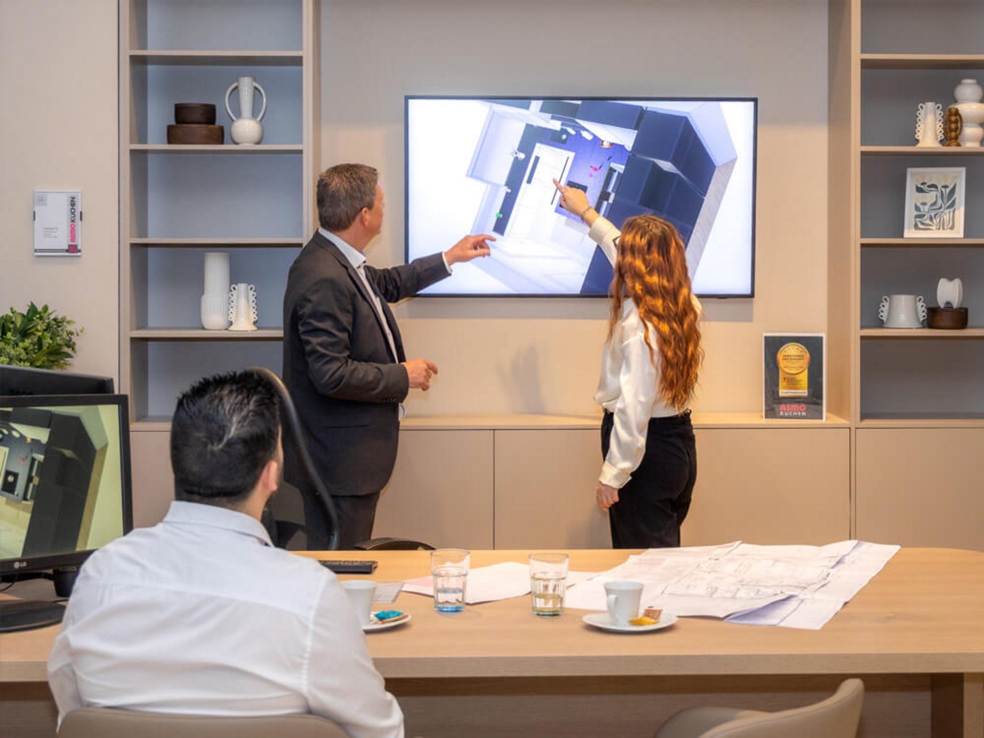 Drei Personen besprechen eine Küchenplanung auf einem großen Bildschirm im Küchenstudio