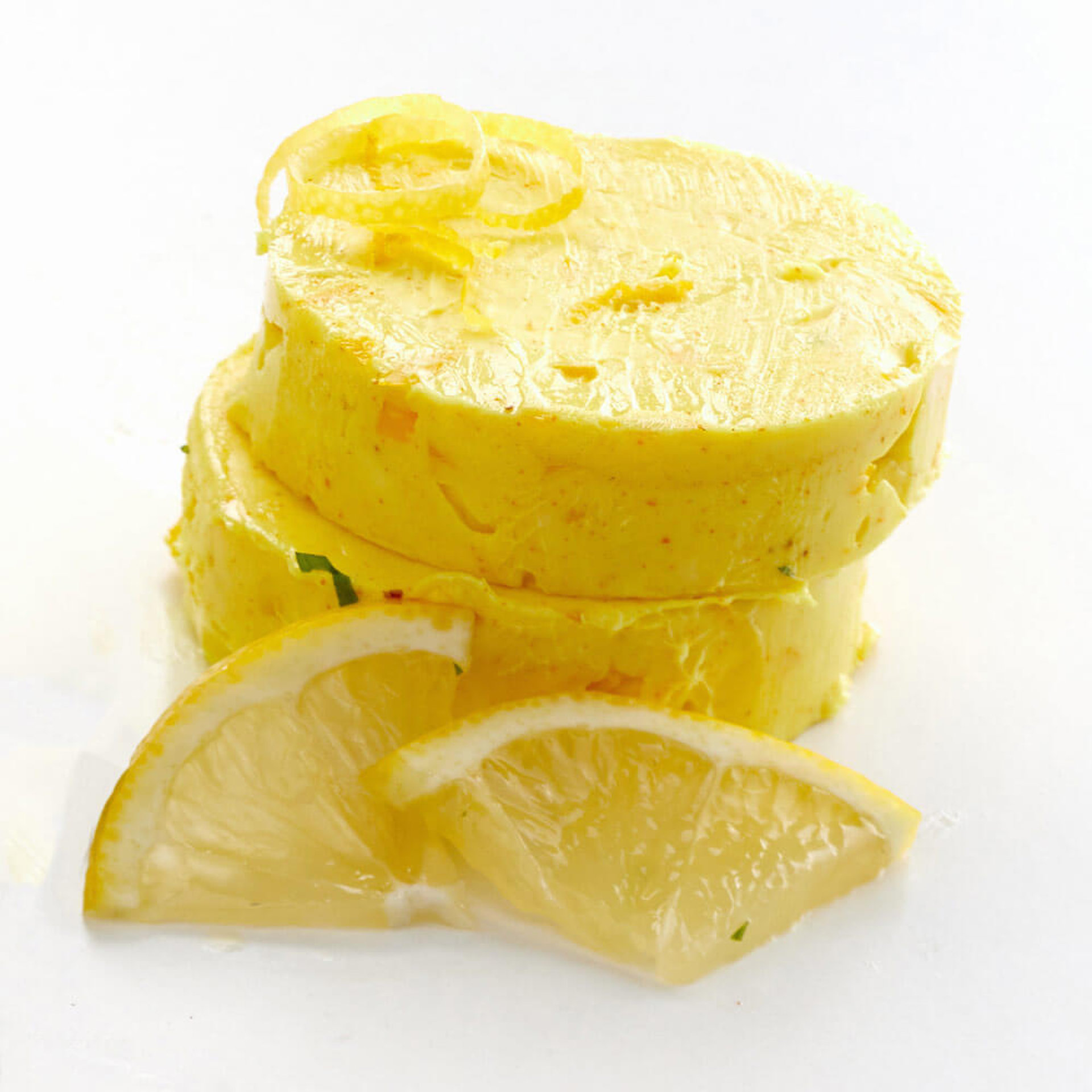 Zwei gestapelte, gelbe Rollen selbstgemachter Zitronen-Butter, garniert mit frischen Zitronenspalten und Zitronenzesten.