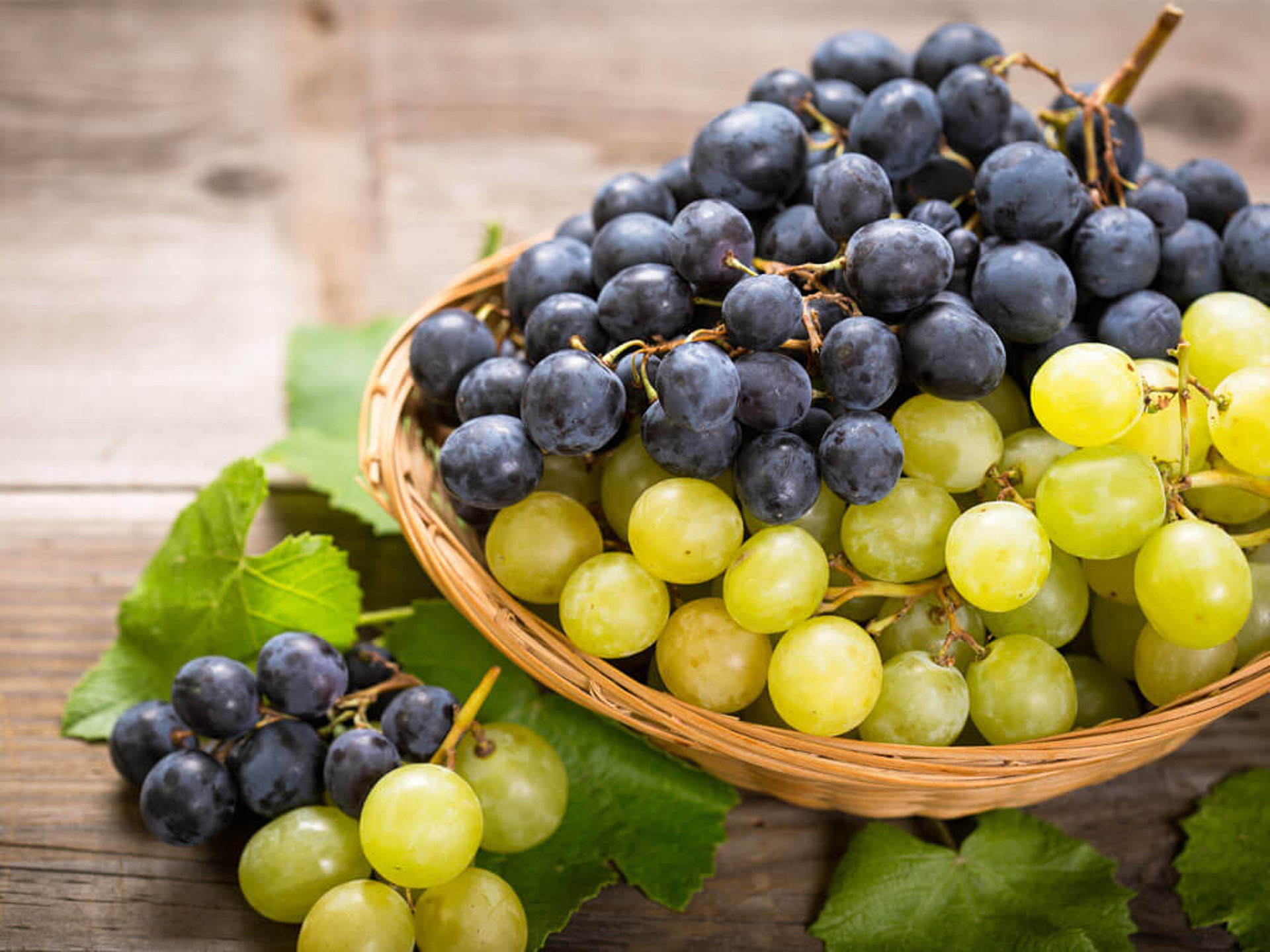 Ein Korb gefüllt mit frischen grünen und blauen Weintrauben auf rustikalem Holzhintergrund – gesunder Snack.