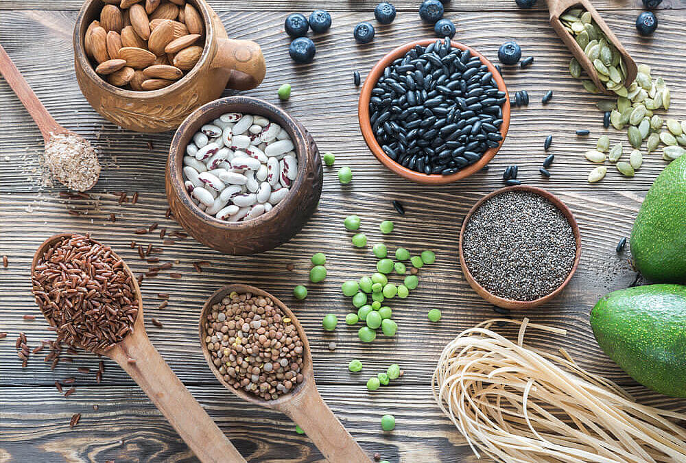 Ballaststoffreiche Lebensmittel wie Nüsse, Hülsenfrüchte, Avocado und Vollkorn-Nudeln auf einem Tisch, ideal für den Fibremaxxing-Trend und eine gesunde Ernährung.