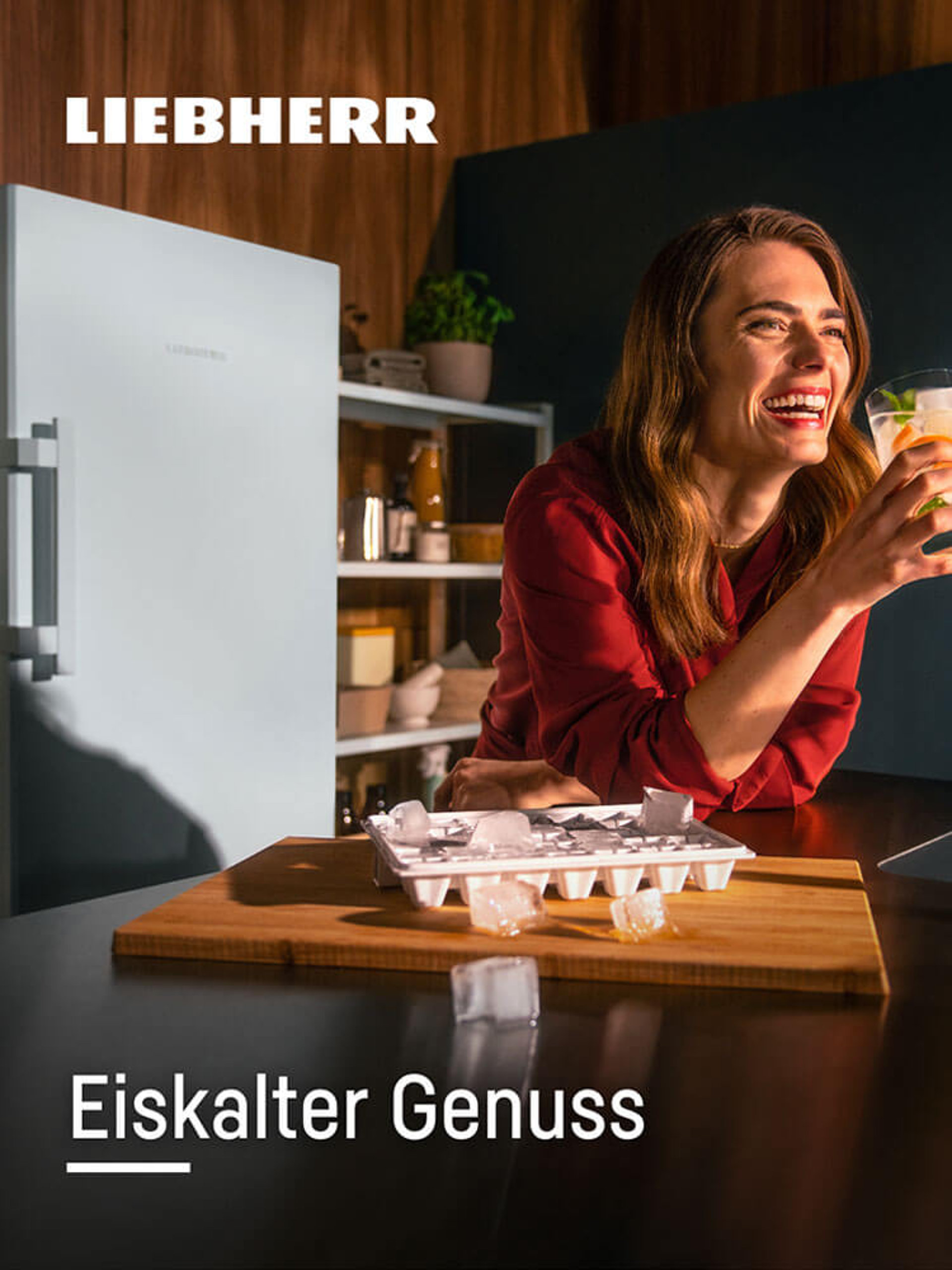 Lachende Frau genießt ein Kaltgetränk, mit Liebherr-Kühlschrank mit Eiswürfelbereiter im Hintergrund.