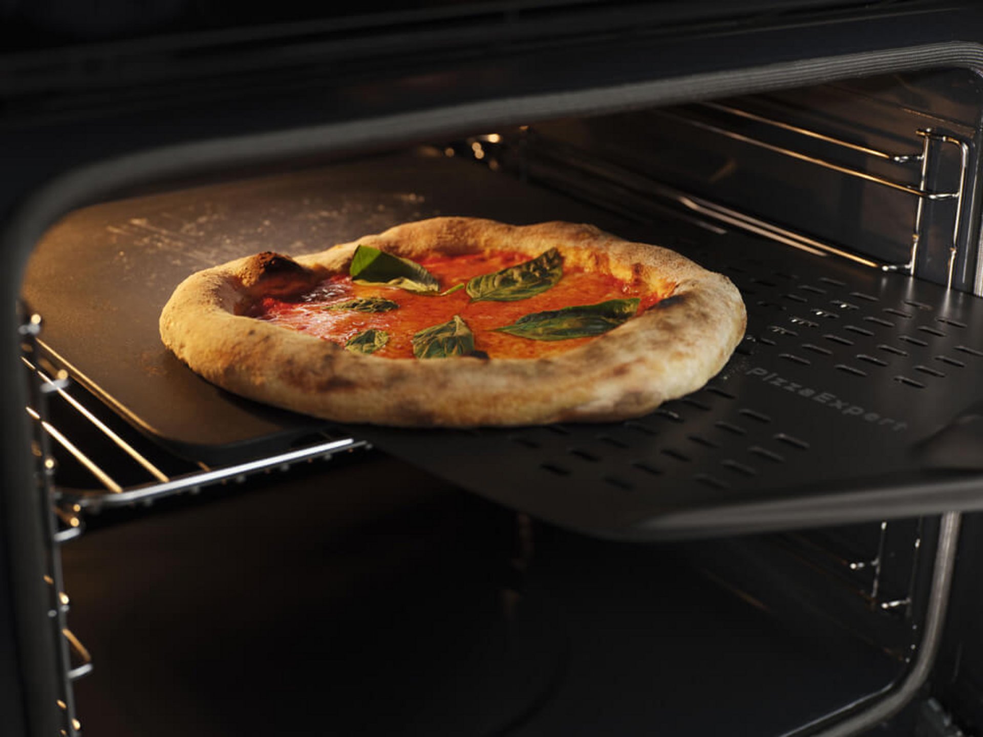 Pizza mit Tomatensauce und Basilikum backt auf der PizzaExpert-Platte im geöffneten Backofen