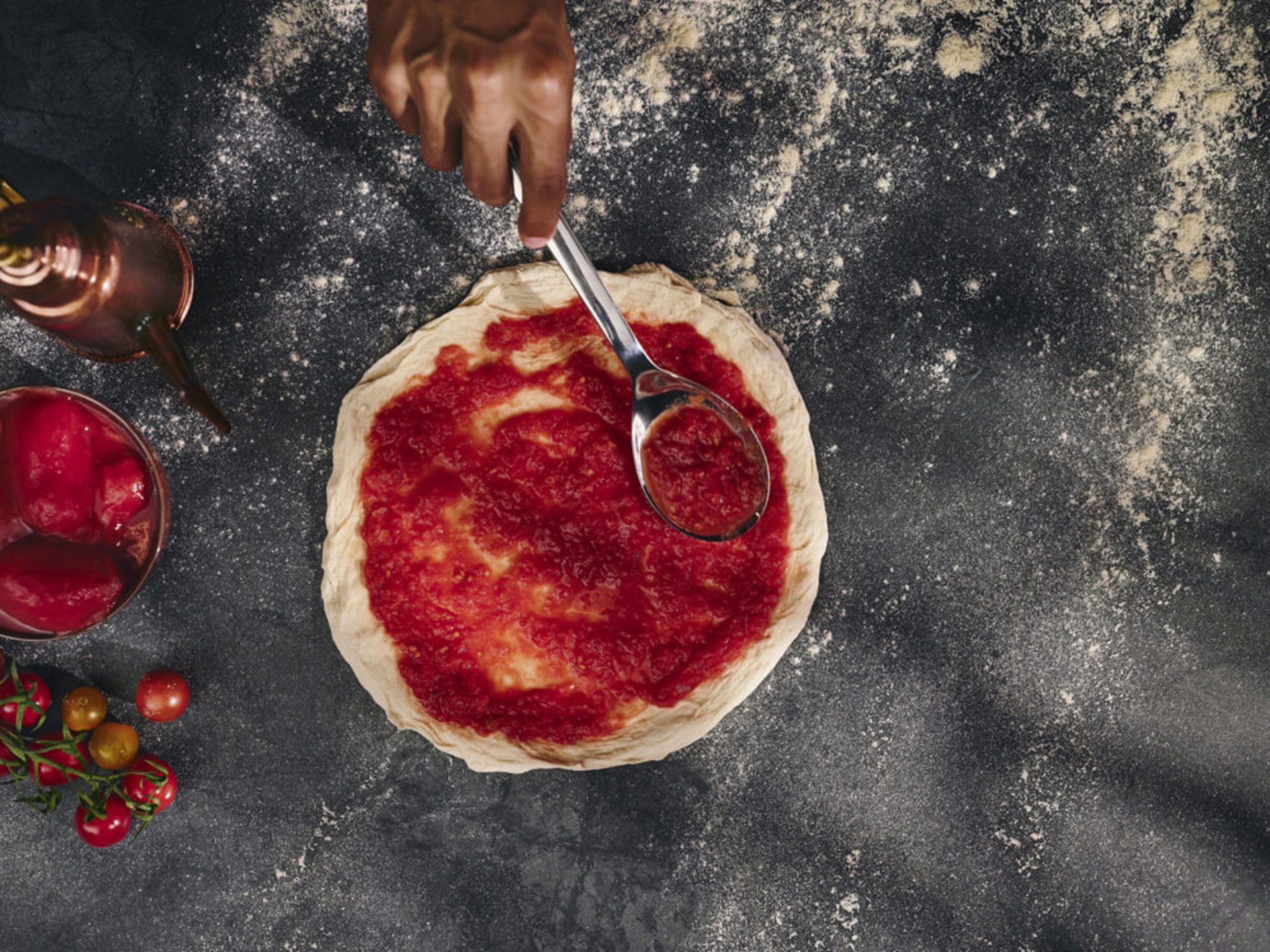 Tomatensauce wird mit einer Kelle auf rundem Pizzateig verteilt