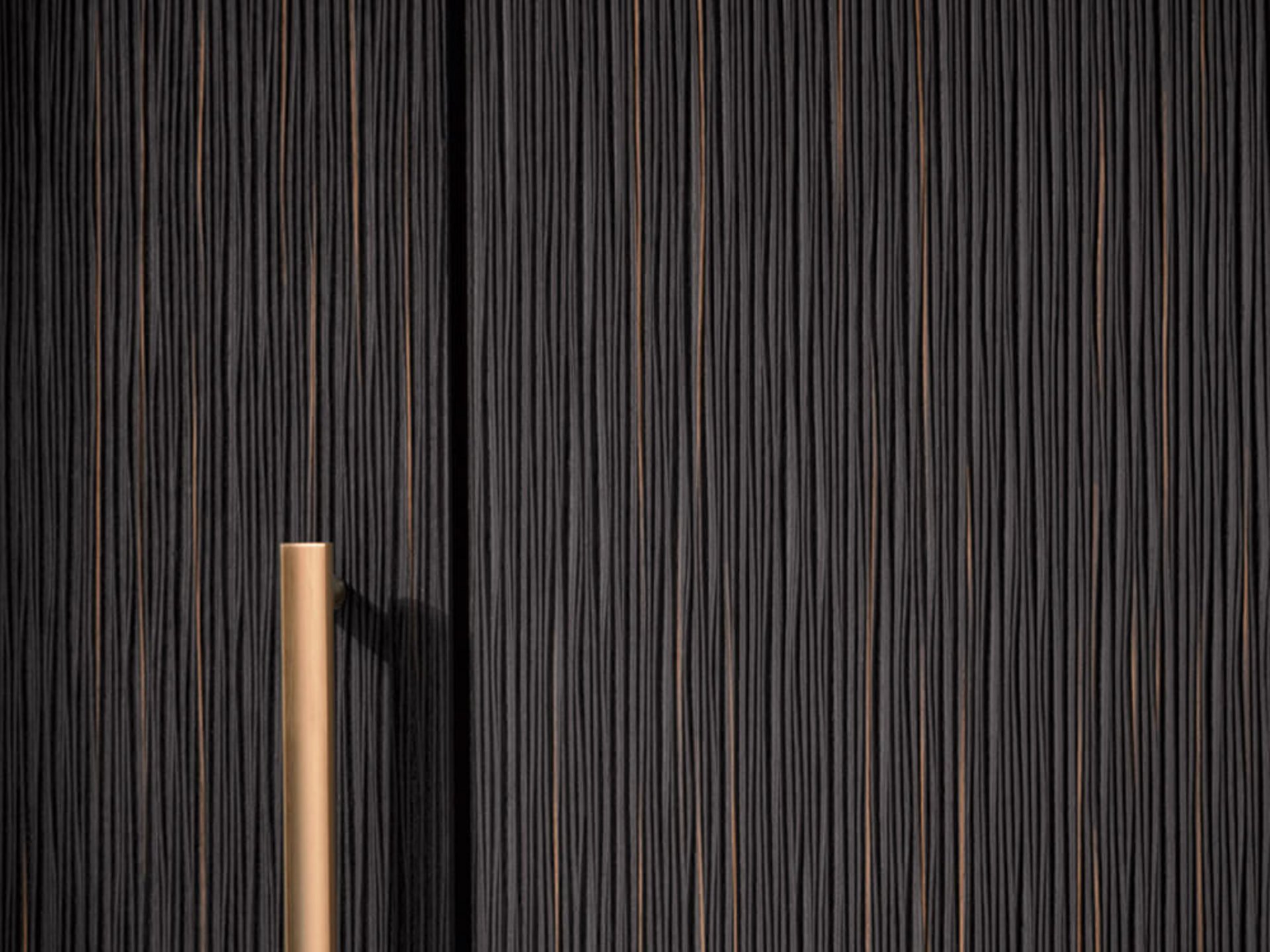 Detail einer schwarzen Front in Riffeloptik mit bronzefarbenem Griff.