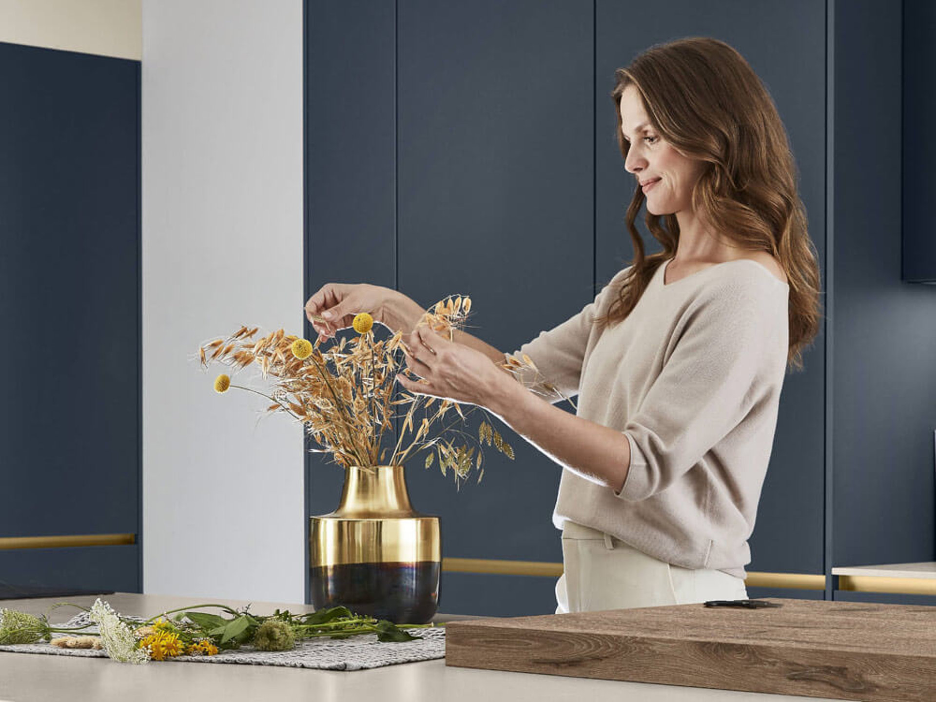 Eine Frau dekoriert eine moderne Küche mit ultramatten, pflegeleichten Anti-Fingerprint Fronten in Marineblau.