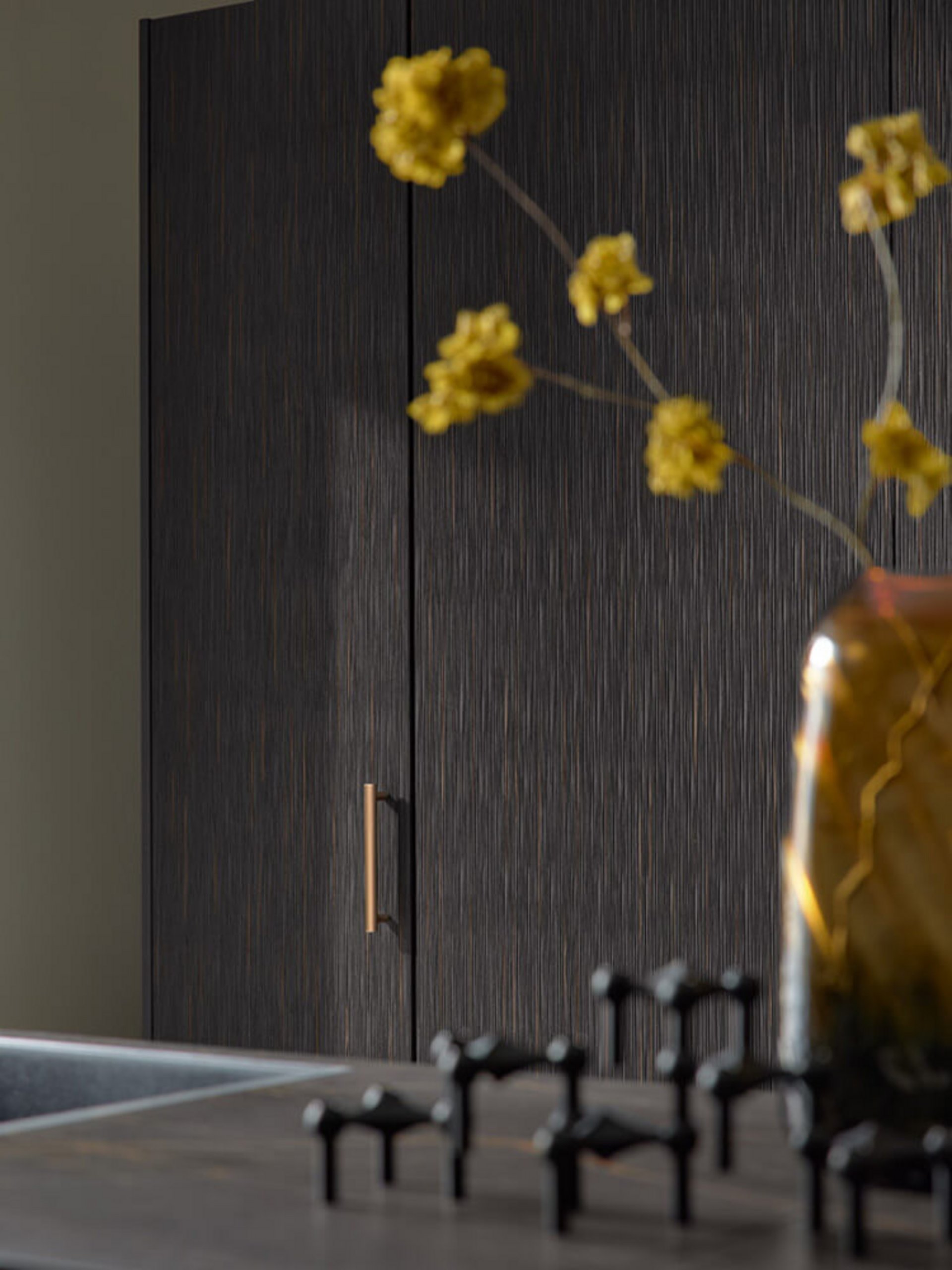 Organische Küchenfront in Bernstein-Schwarz mit dekorativer Vase und fühlbarer Riffelstruktur.