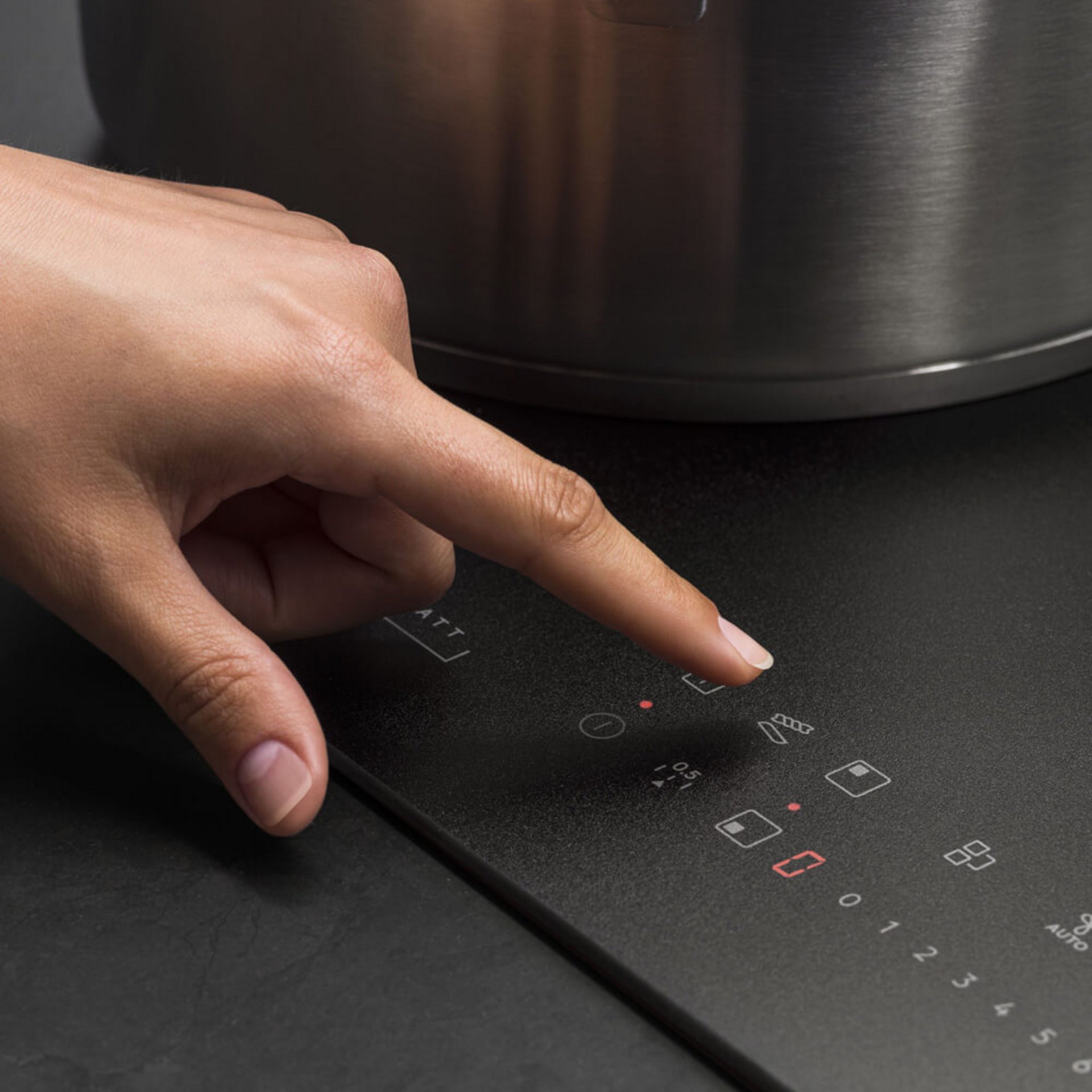 Hand bedient das Touchfeld eines AEG Kochfelds neben einem Topf