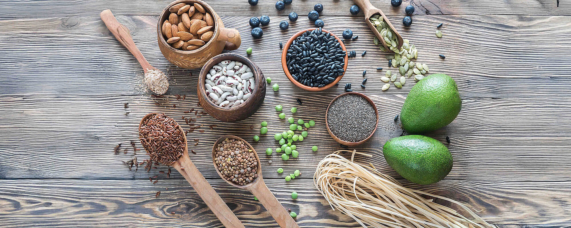 Ballaststoffreiche Lebensmittel wie Nüsse, Hülsenfrüchte, Avocado und Vollkorn-Nudeln auf einem Tisch, ideal für den Fibremaxxing-Trend und eine gesunde Ernährung.