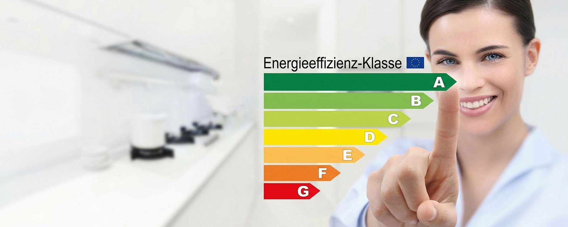 Frau zeigt auf eine farbige Skala zur Energieeffizienz vor einer Küche