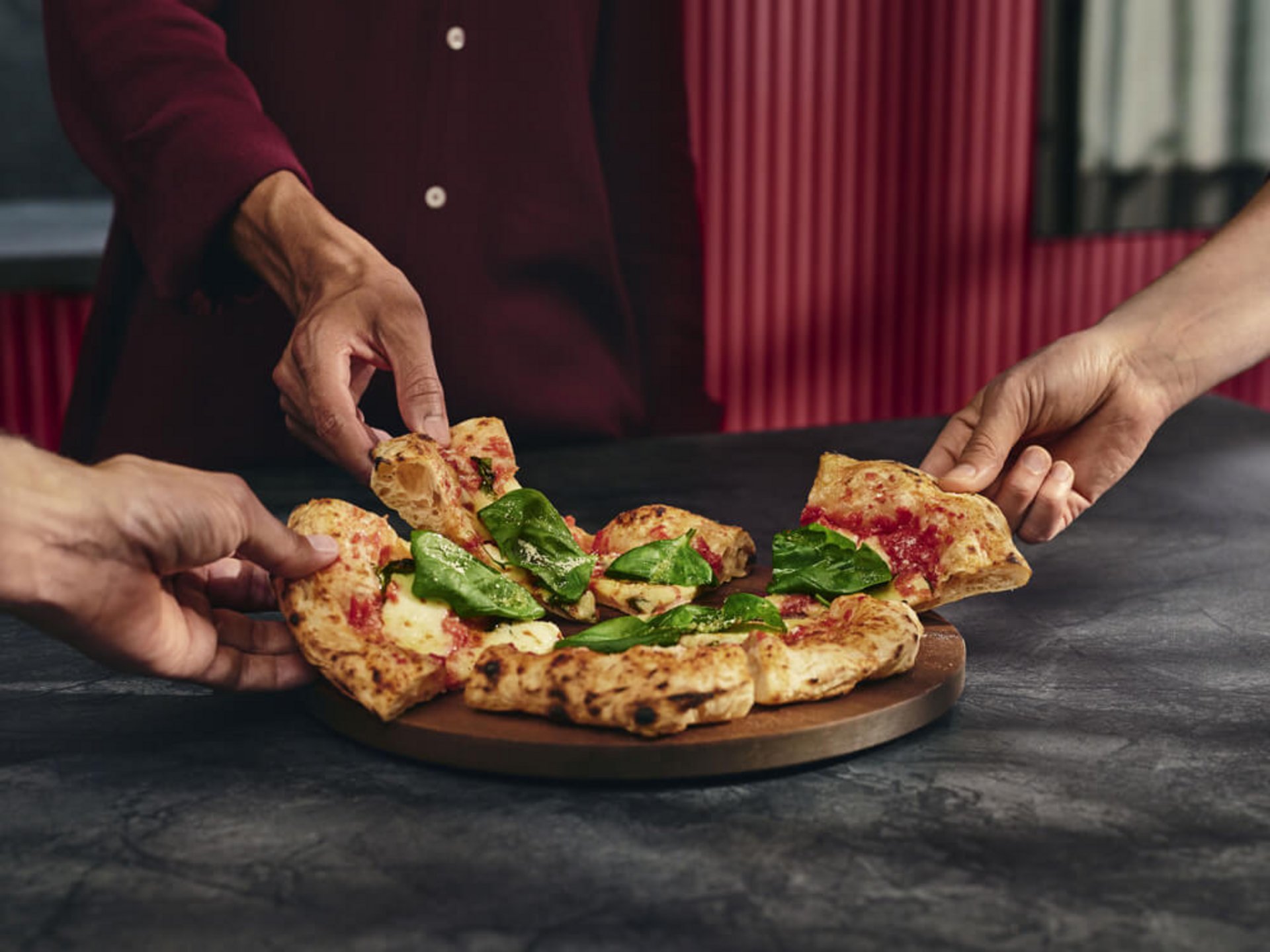 Mehrere Personen nehmen Stücke einer geschnittenen Pizza Margherita von einem Holzbrett