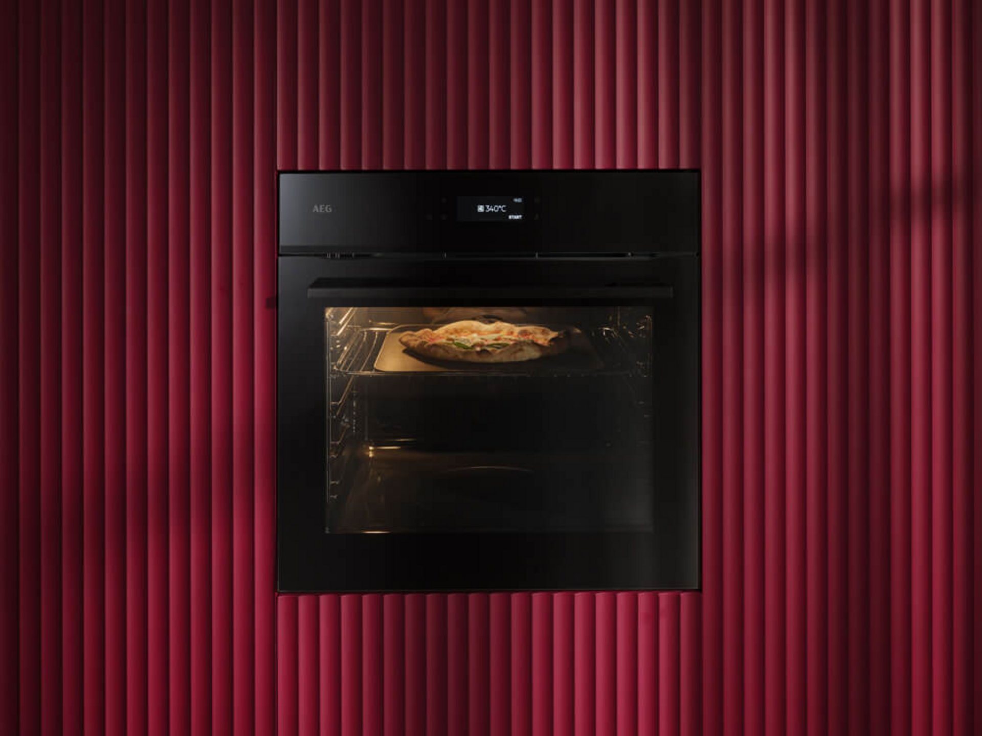 Schwarzer AEG PizzaExpert Backofen mit Pizza vor einer roten geriffelten Küchenfront