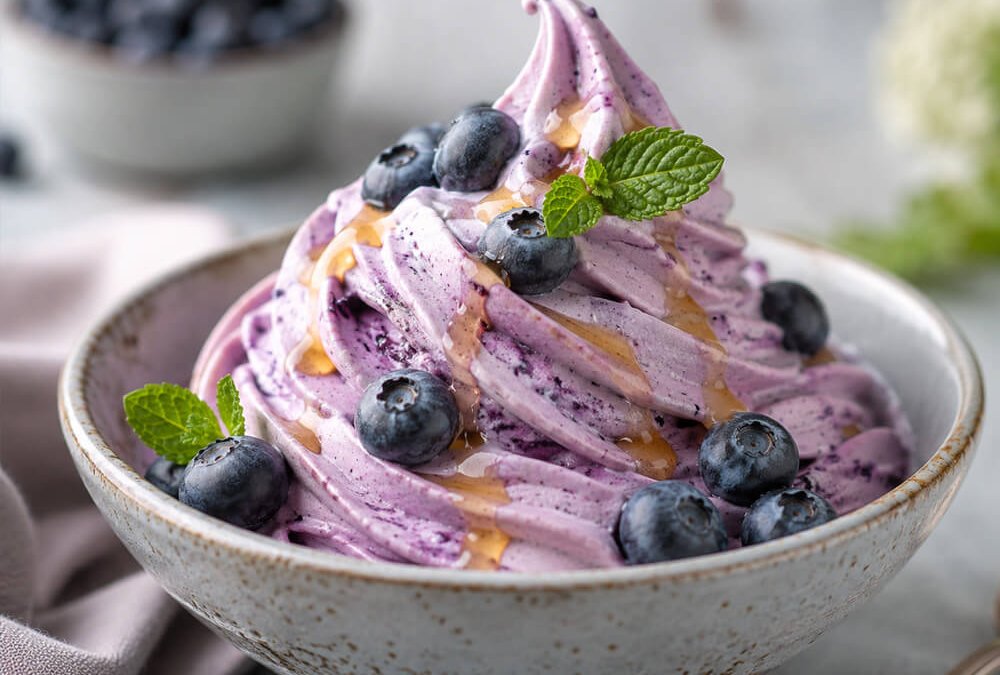 Cremiges Blaubeer-Softeis mit Topping in einer Schale angerichtet