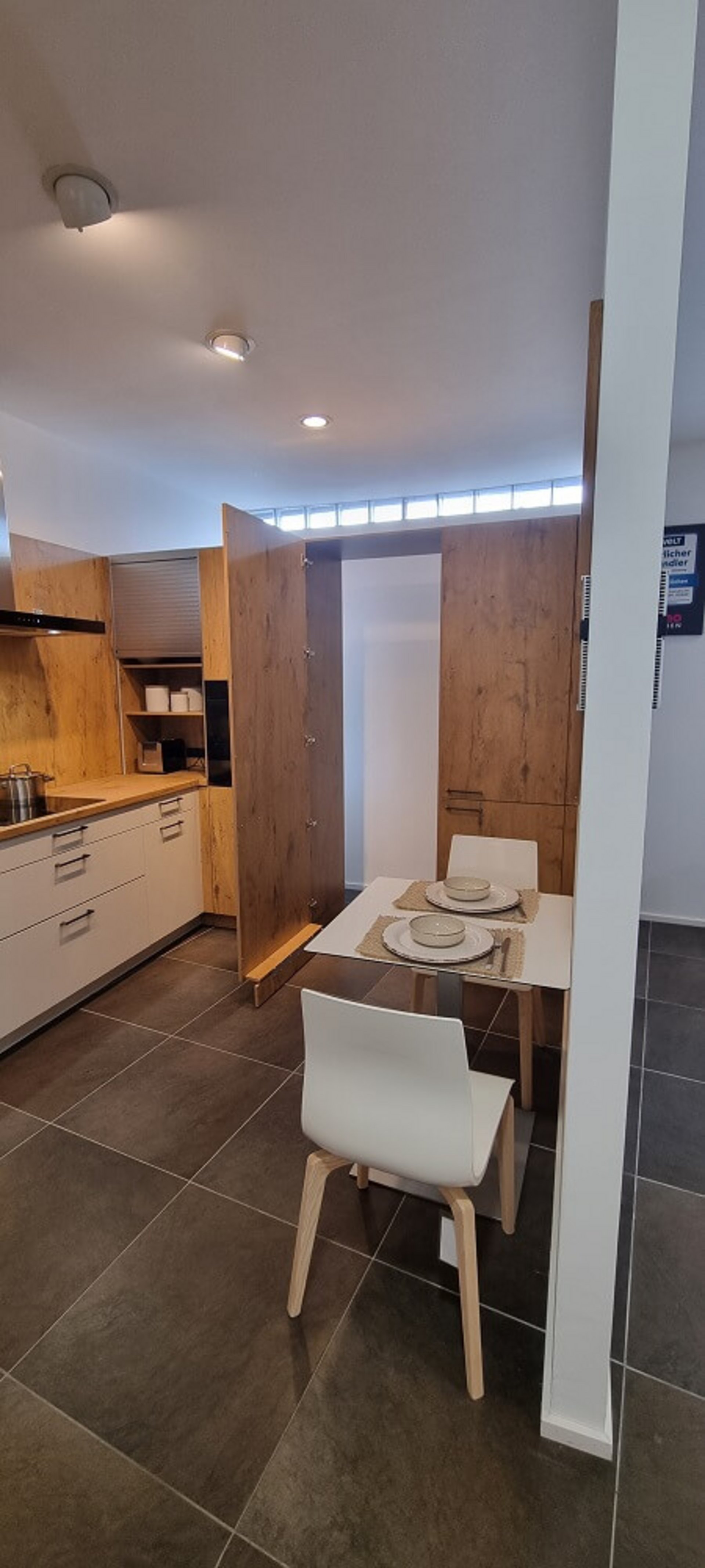 Küche Cantania in Eiche hellgrau mit weißer Unterschrankzeile, gemusterter Nischenrückwand und angrenzendem Essplatz im Studio von ASMO KÜCHEN Landshut.