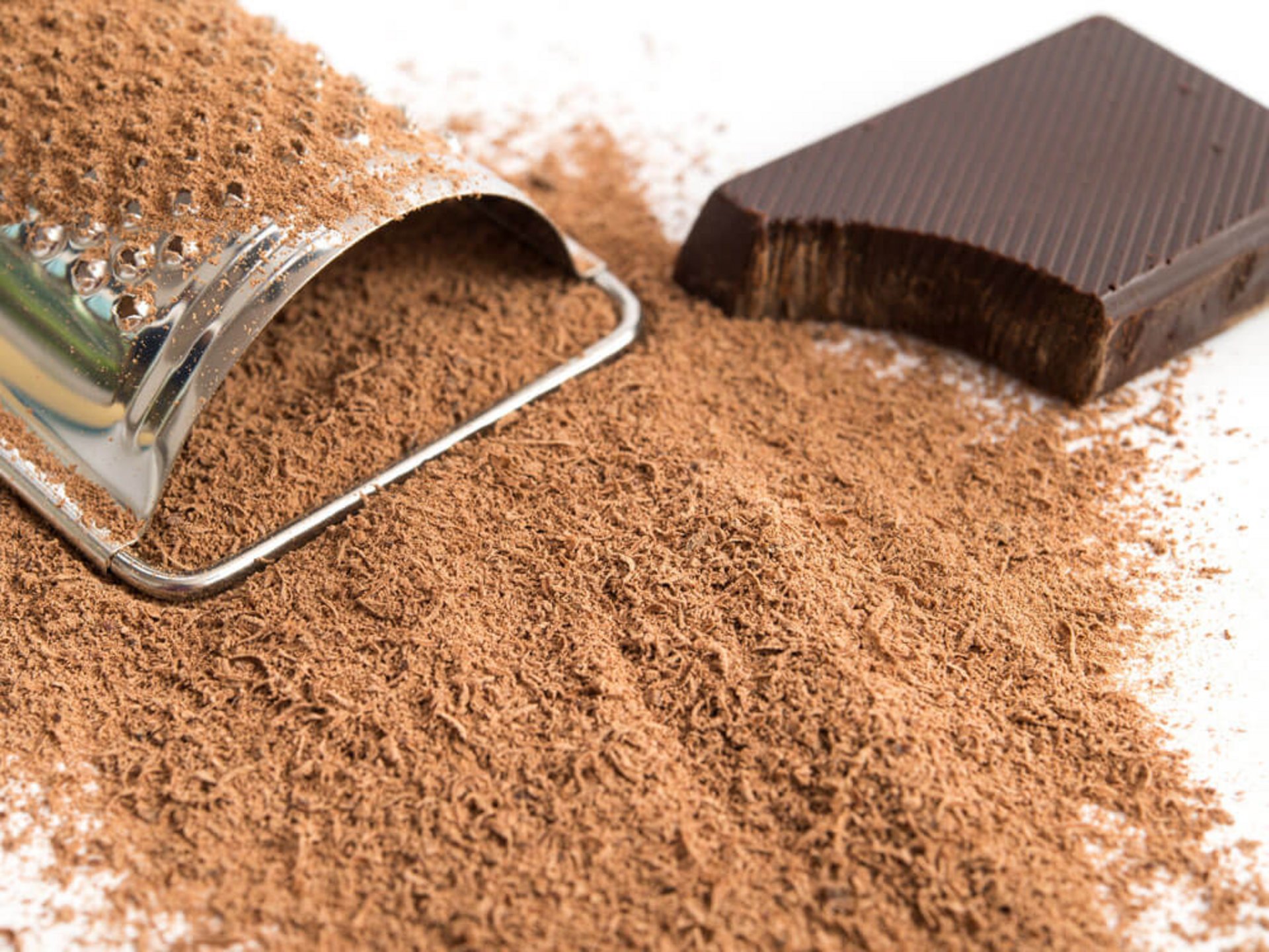 Fein geraspelte Schokolade als braunes Pulver neben Küchenreibe – Schokolade raspeln als Topping