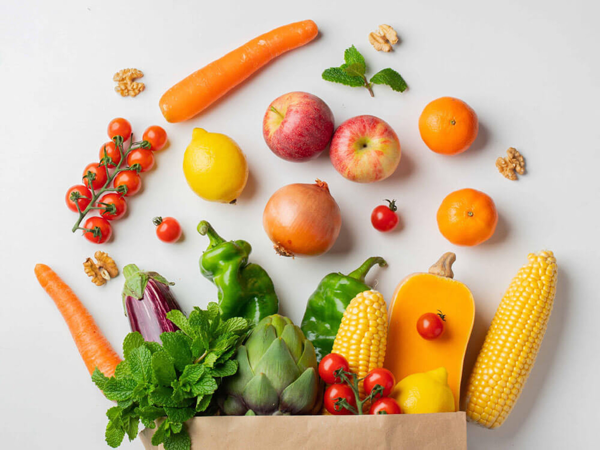 Frisches Obst und Gemüse wie Äpfel, Karotten und Tomaten in einer Papiertüte, um Ballaststoffe zu steigern und einen gesunden Snack zu machen.