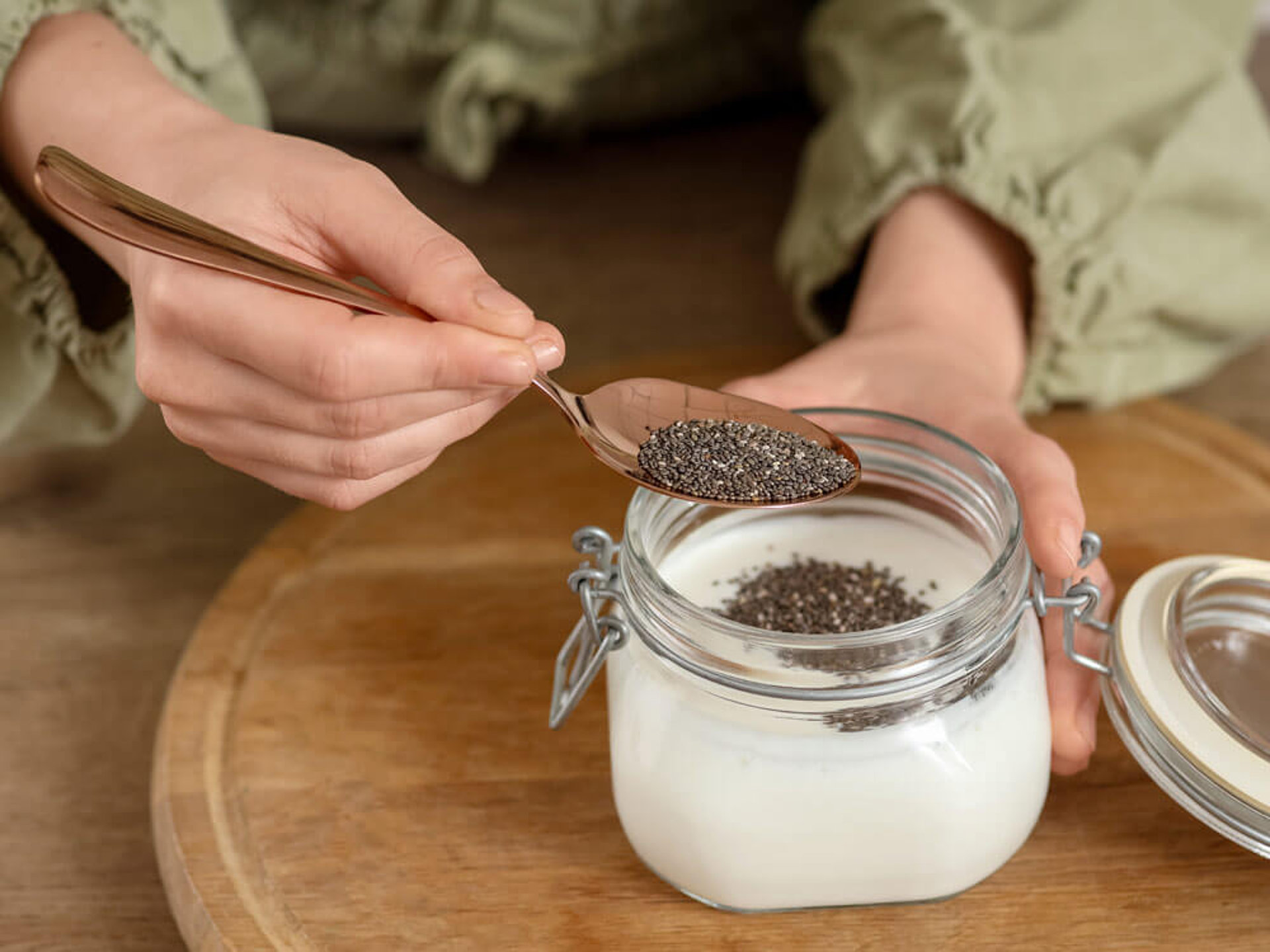 Hände streuen Bio Chiasamen in Joghurt. Optimale Chiasamen Dosierung für Pudding und tägliche Anwendung.