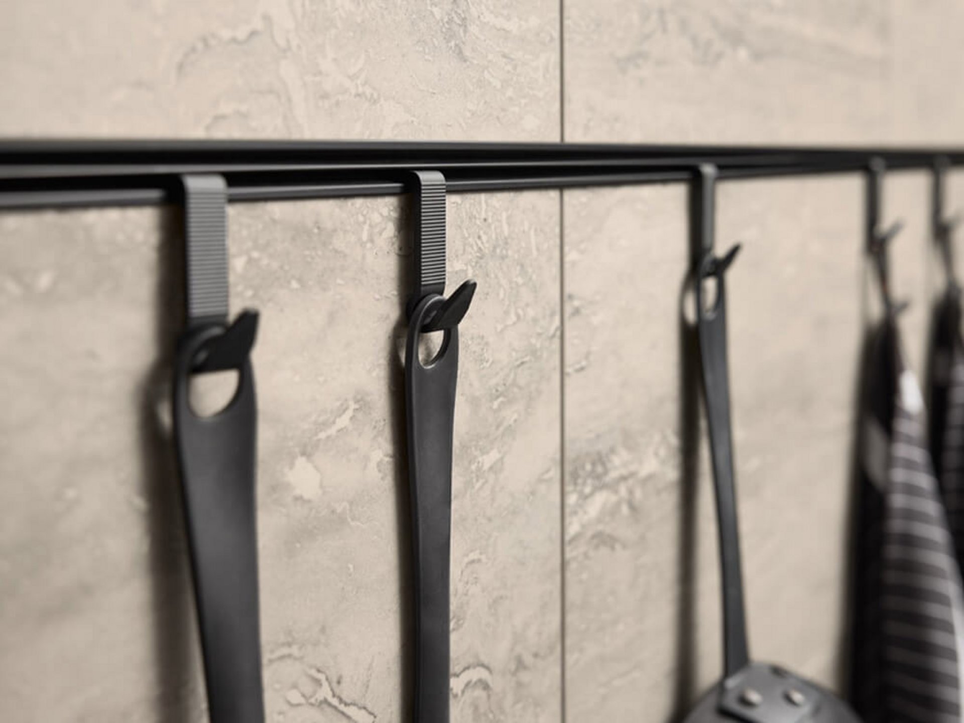 Relingleiste mit Haken für Küchenutensilien an einer Wandpaneele in Steinoptik