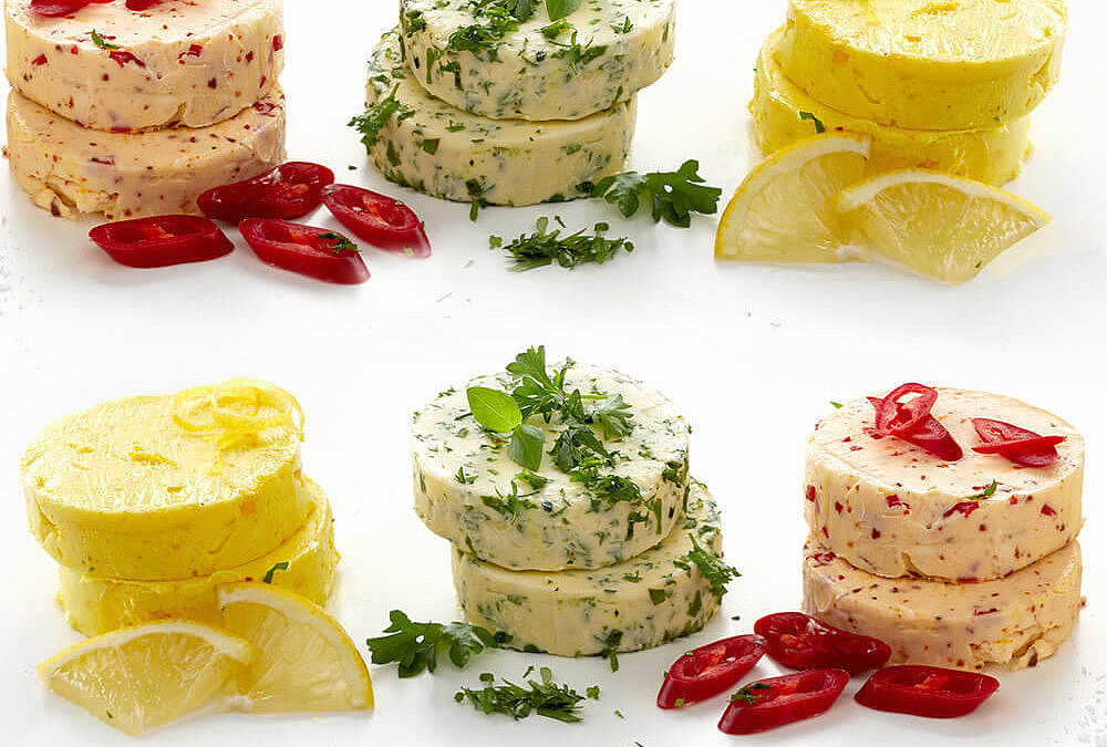 Vier verschiedene selbstgemachte Grillbutter, darunter Kräuter-Butter, Chili-Butter, Zitronen-Butter und einfache Butter mit Pfeffer.