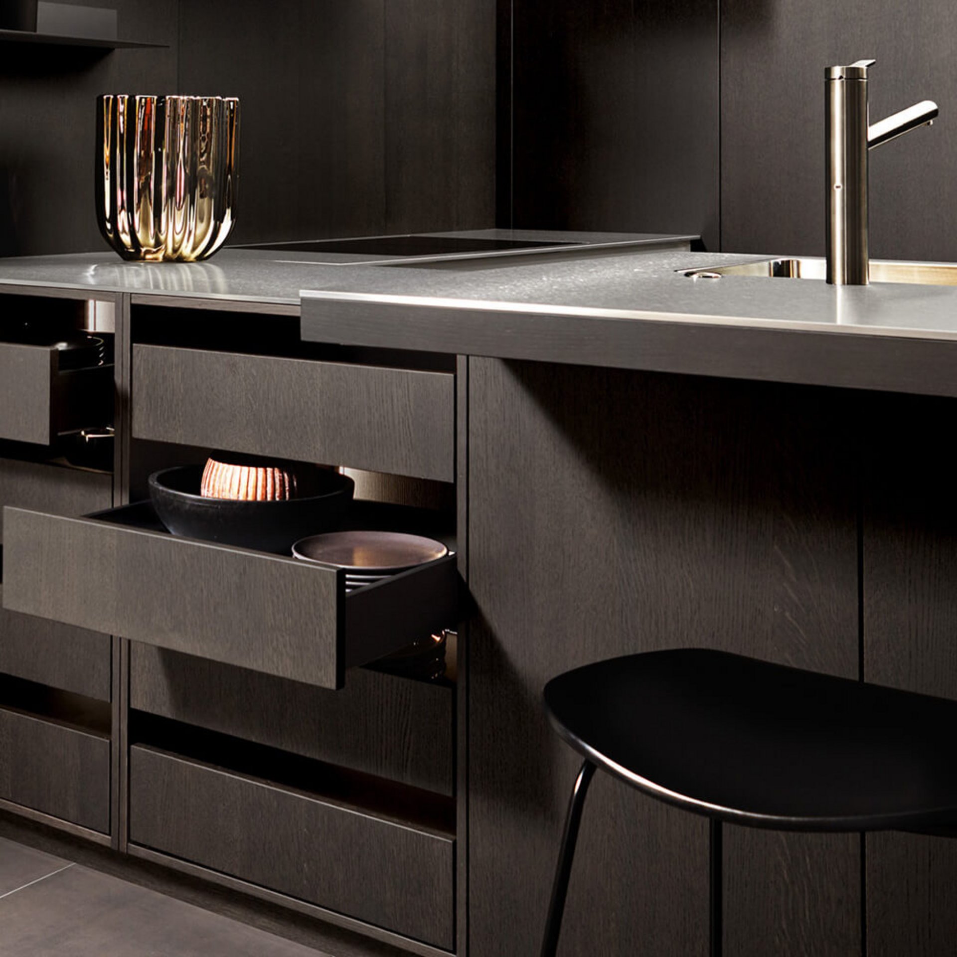 Dunkle Holzküche in Eiche Trüffelgrau mit Naturstein-Arbeitsplatte, Armatur und geöffneten Auszügen als Stauraumdetail.