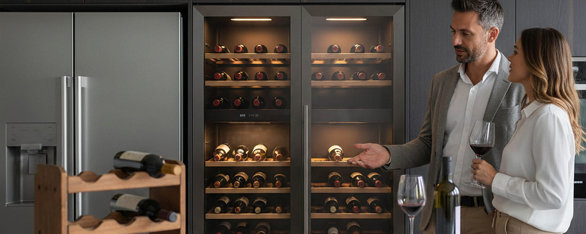 Weinliebhaber-Paar in der Küche – Mann zeigt auf eingebauten Dual-Zone-Weinkühlschrank, Frau hält Rotweinglas – optimale Weinlagerung und Temperaturkontrolle